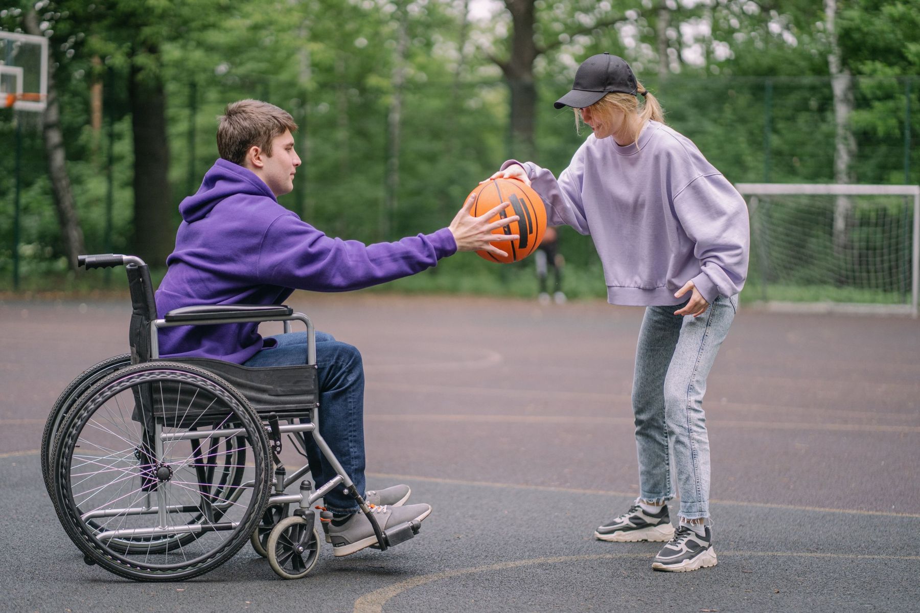 Two people playing basketball outdoors, one of them using a wheelchair