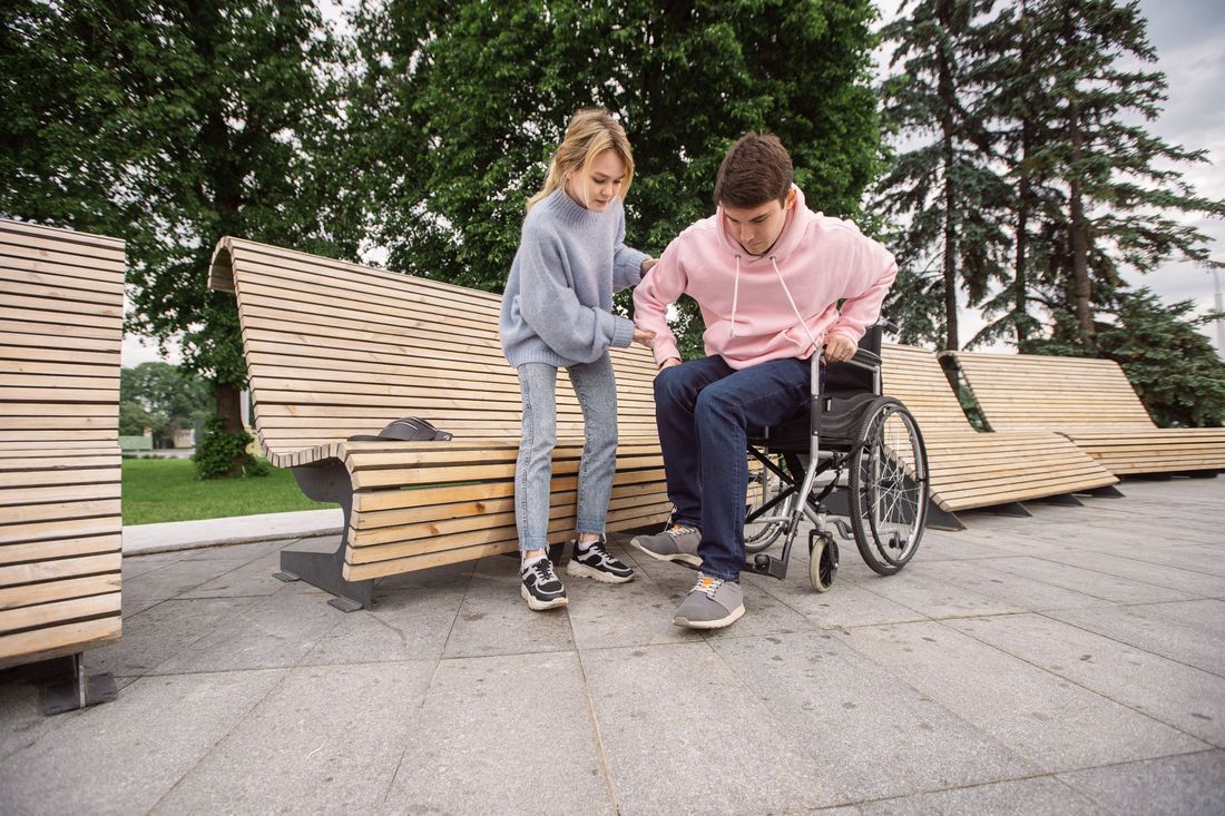 A support worker steadying a man as he moves from a bench into his wheelchair