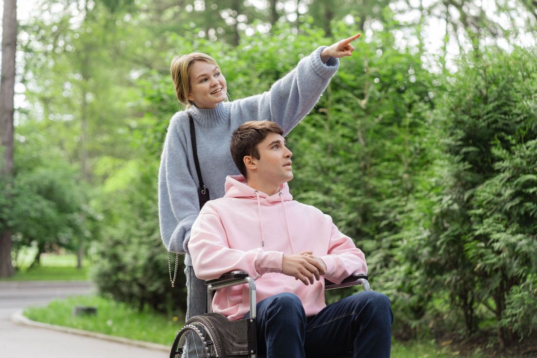 A support worker pointing out something in the distance while walking with a man in a wheelchair