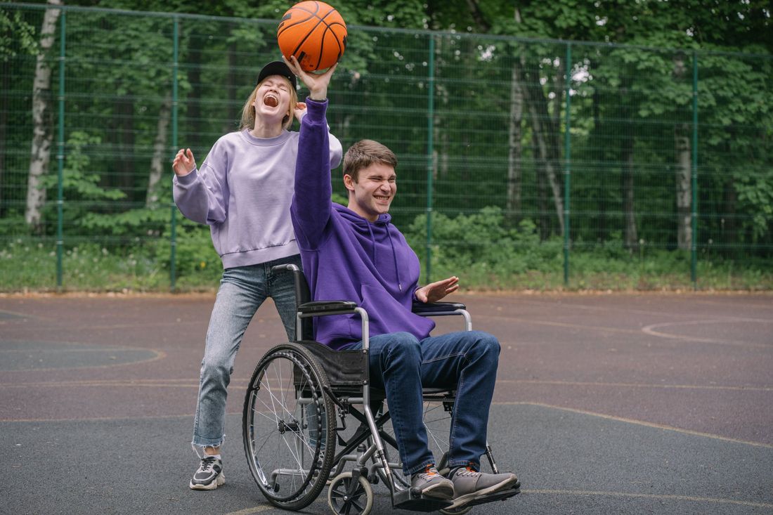 Two people laughing together while playing basketball outdoors